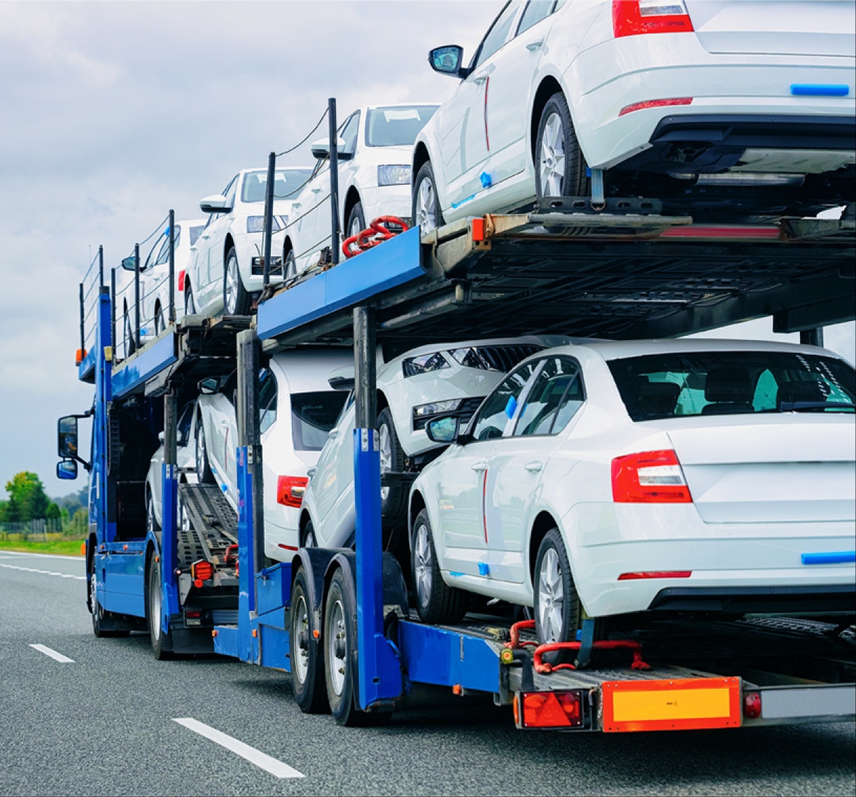 Multi-car carrier trailer transporting white sedan cars on a highway.